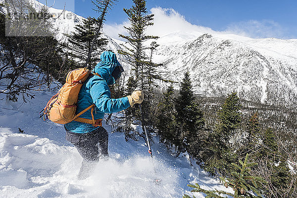 Eine Frau  die allein einen verschneiten Hang hinunterwandert  mit der Tuckerman-Schlucht und dem Gipfel des Mount Washington im Hintergrund.
