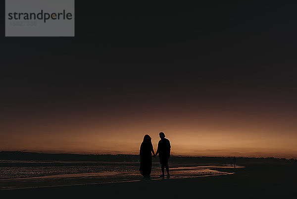 Silhouette von Mann und Frau beim Spaziergang am Strand bei Sonnenuntergang