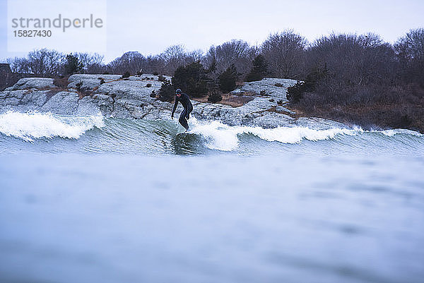 Mann surft auf kleinen Winterwellen an bedecktem Tag