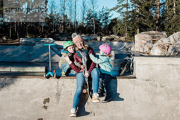 Mama und ihre Kinder haben Spaß in einem Skatepark mit Fahrrädern und Rollern