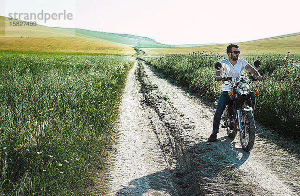 junger Mann parkt sein Motorrad auf der grünen Wiese  um nachzudenken