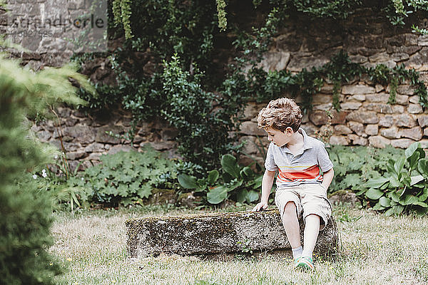 Frontansicht eines Jungen  der auf einer mit Moos bewachsenen Felsbank sitzt