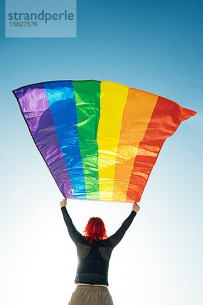 Frau hält die schwule Regenbogenfahne auf blauem Himmelshintergrund. Glück  Freiheit und Liebeskonzept für gleichgeschlechtliche Paare.