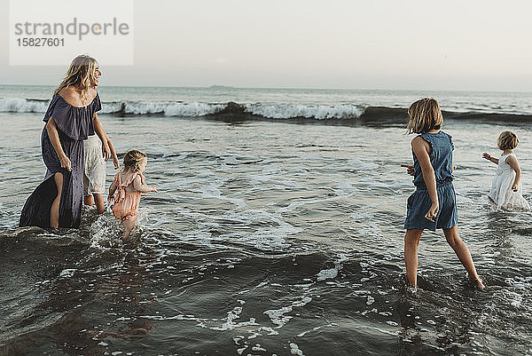 Starke Mutter mit vier Töchtern  die bei Sonnenuntergang im Meer spielen
