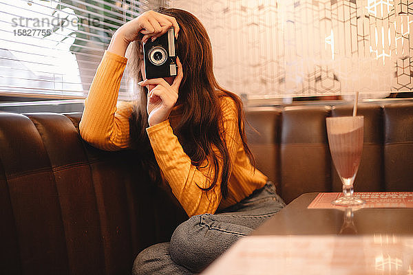 Junge Frau fotografiert mit einer Oldtimer-Kamera  während sie im Café sitzt