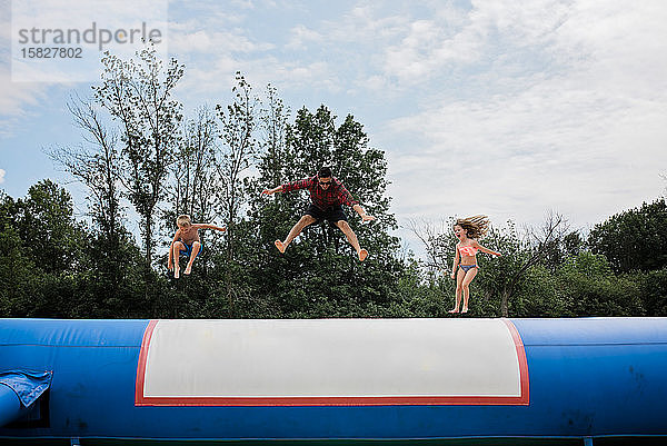 Junger Erwachsener und zwei Kinder springen an einem sonnigen Tag gegen den blauen Himmel