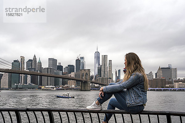 Attraktive junge Frau beobachtet die Brooklyn Bridge vom Hudson River in New York City