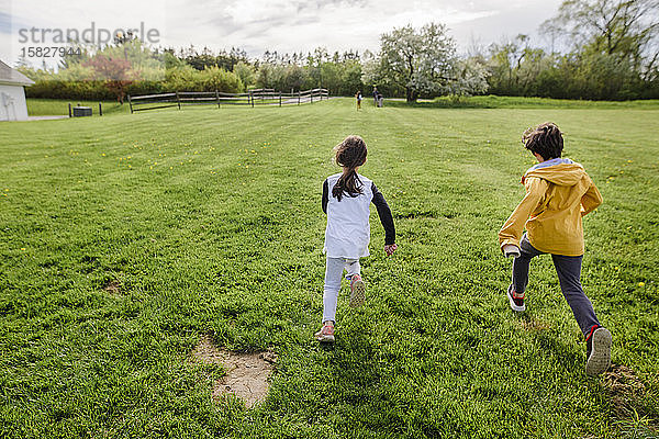 Drei Kinder rennen im Frühling durch ein Feld  eines weit voraus