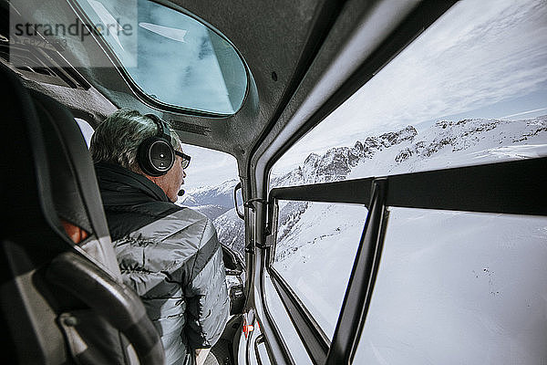 Hubschrauberpilot schaut aus dem Seitenfenster  während er über den Alpensee fliegt.