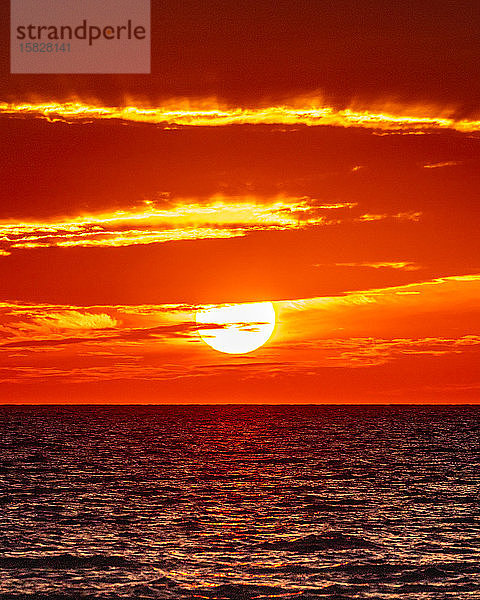 Die Sonne geht entlang des Ozeanhorizonts unter und lässt die Wolken mit Feuer lodern.