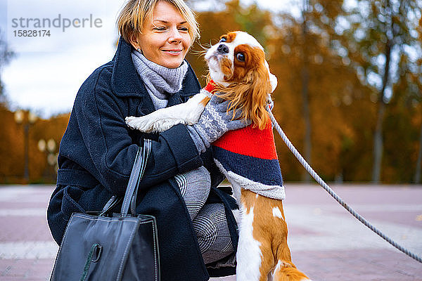 Frau bei einem Spaziergang im Park mit einem Hund von Cavalier King Charles Spaniel.