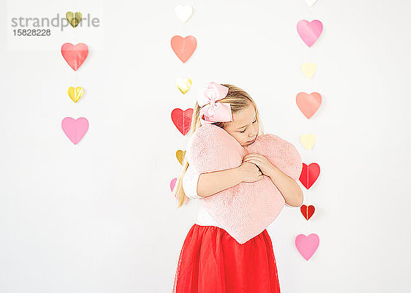 süßes blondes Mädchen umarmt Plüsch rosa Herz Valentinstag