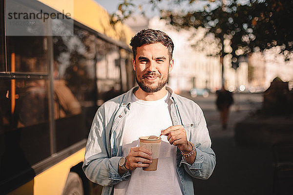 Glücklicher Mann hält im Sommer eine Tasse Kaffee in der Hand  während er auf der Straße steht