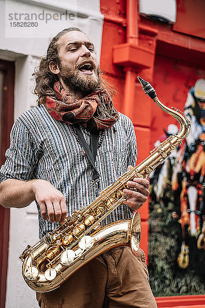 Vertikales Foto eines Saxophonisten  der mit emotionalem Ausdruck auf der Straße singt