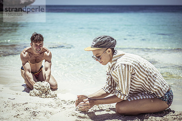 junger Mann und Frau bauen Sandburgen am unberührten blauen Strand in der Sonne