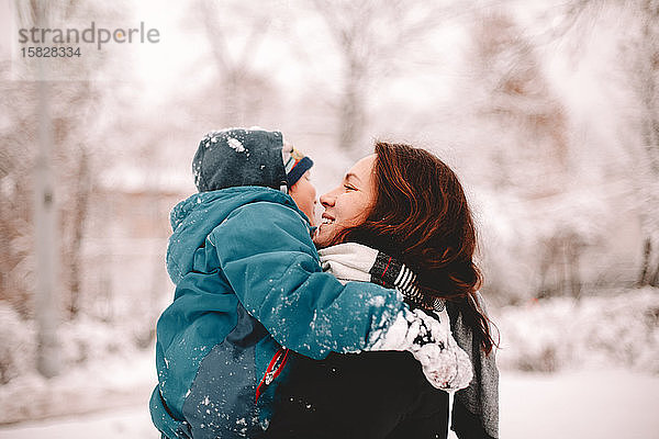 Glückliche Mutter hält Sohn  während sie im Winter im Park steht