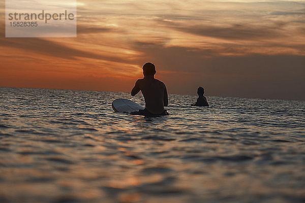 Zwei Surfer im Ozean bei Sonnenuntergang