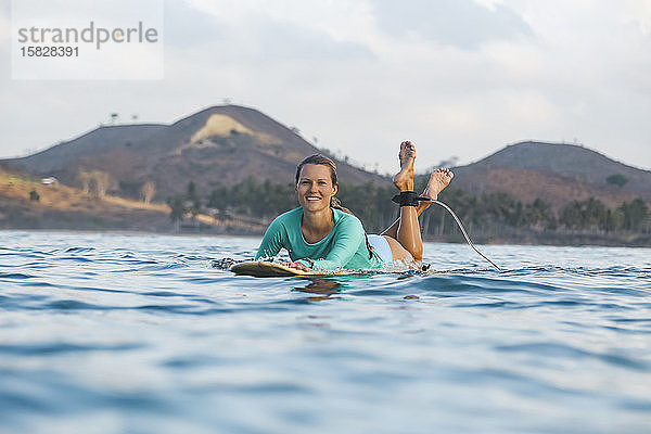 Lächelnde junge Frau auf dem Surfbrett liegend