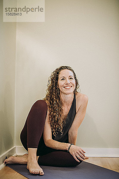 Porträt einer lächelnden Frau in Yogakleidung auf einer Matte in einem Studio