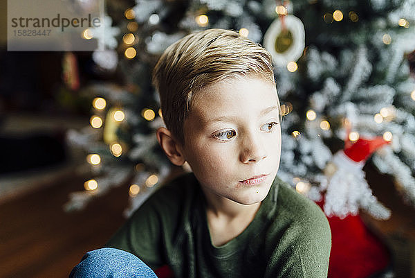 Junge schaut aus dem Fenster neben dem Weihnachtsbaum