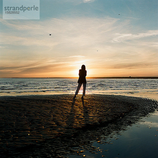 Schöne Frau steht am Meer und genießt den Sonnenuntergang