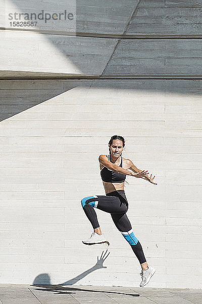 Ganzkörper einer Athletin in Sportkleidung springt auf Beton