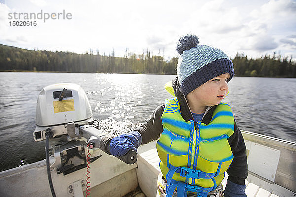 Ein Junge fährt an einem sonnigen Tag auf einem ruhigen See ein Motorboot.