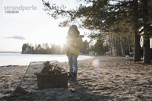 Junge stand neben einem Feuer am Strand in Schweden