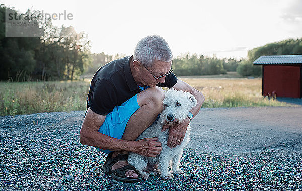 Porträt eines Mannes  der im Sommer beim Spaziergang mit einem Hund kuschelt