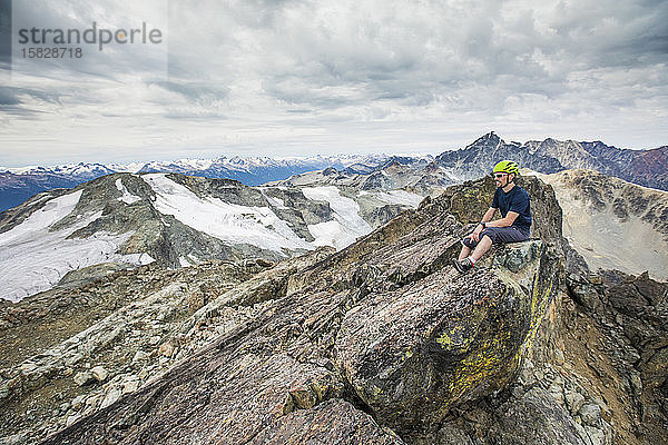 Bergsteiger sitzt auf dem felsigen Gipfel eines Berges.