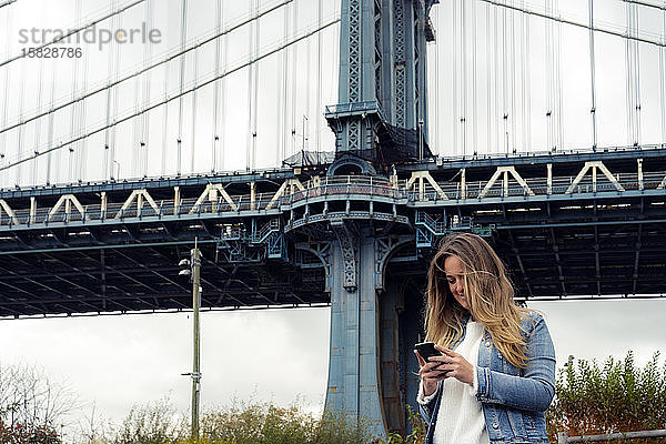 Attraktive Frau benutzt ihr Smartphone auf der Manhattan Bridge