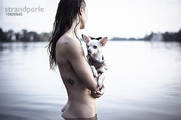 starke frau mit tatoo hält zwei kleine hunde im natürlichen berliner see