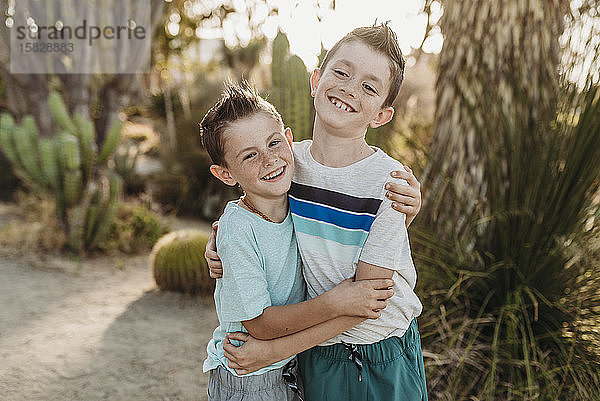 Fröhliche Brüder umarmend und lächelnd im sonnigen Kaktusgarten