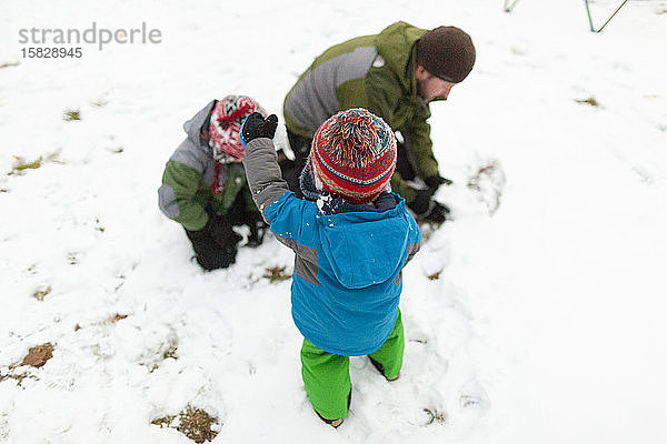 Vater macht im Winter mit zwei Kindern draußen einen Schneeball