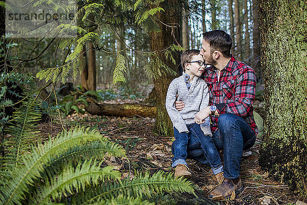 Vater küsst jungen Sohn im Wald auf die Stirn.