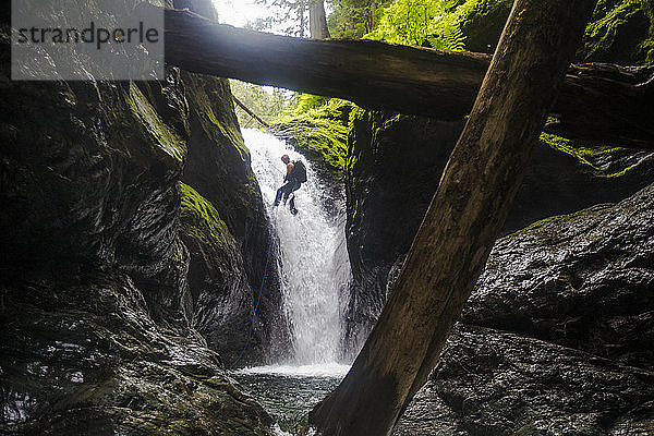 Tiefblick auf einen Mann  der sich von einem Wasserfall abseilt.