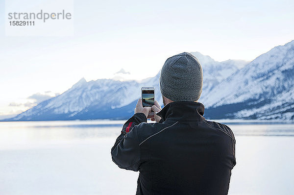 Mann macht mit einem Smartphone ein Foto von Jackson Lake und Teton Range