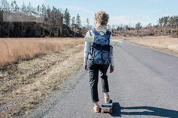 Frau  die eine Yogamatte in einem Rucksack trägt  während sie auf einem Skateboard Schlittschuh läuft