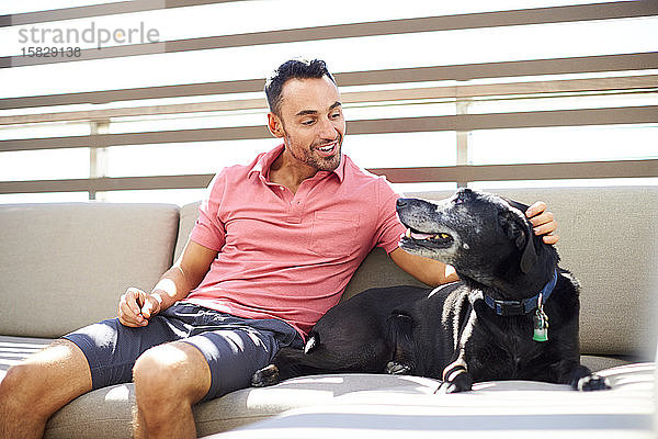 Ein Mann entspannt sich mit seinem Hund auf einer Couch im Freien.
