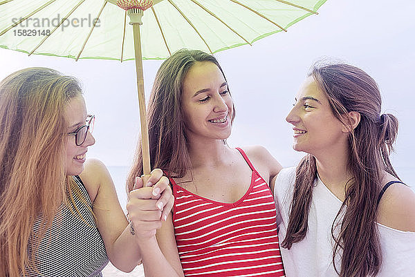 Glückliche junge Frauen haben Spaß am Strand unter einem Sonnenschirm