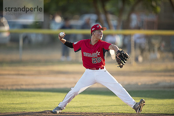 jugendlicher Baseball-Pitcher in roter Uniform in vollem Wind auf dem Hügel