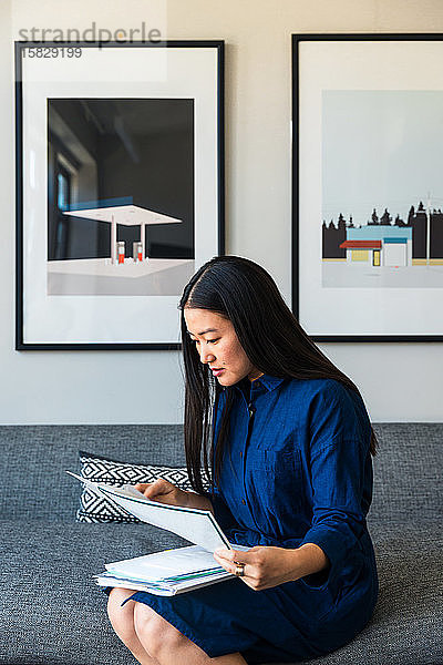 Junge Geschäftsfrau liest Dokumente  während sie im Büro auf dem Sofa sitzt