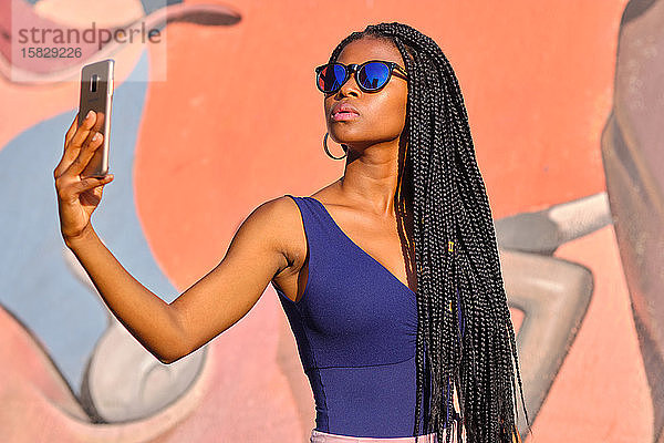 junge schwarze Frau mit sehr langen Zöpfen und sehr attraktiv und sinnlich genießt barcelona im Sommer und macht Model mit Handy  Brille und Kamera  Technikkonzept.