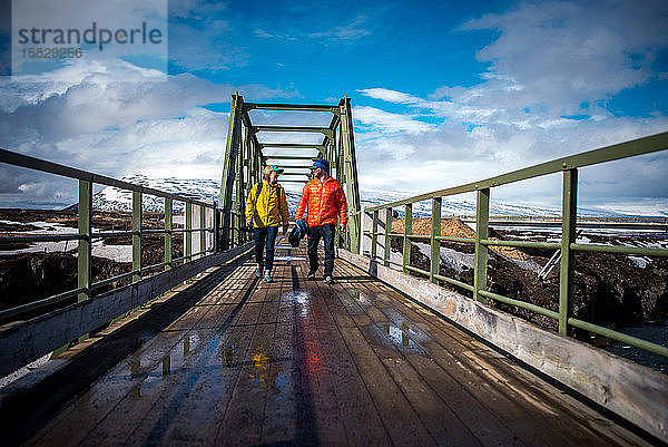 Mann und Frau in Jacken gehen in Island über die Brücke