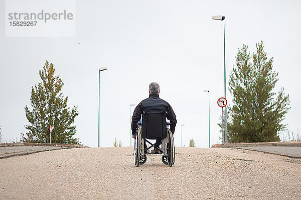 Rückansicht eines behinderten Mannes in einem Rollstuhl allein auf der Straße