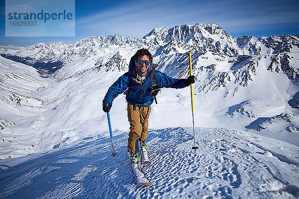 Lächelnder Mann fährt Skitouren auf einer Piste mit Bergen im Rücken