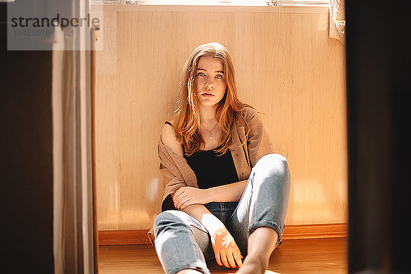 Süße junge Frau  die im Sommer auf dem Boden auf dem Balkon sitzt