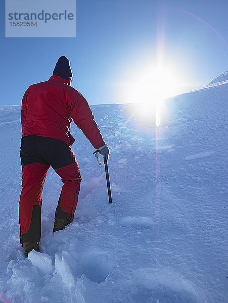 Mann wandert auf verschneiten Hügel einem Gipfel entgegen