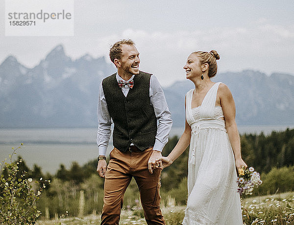 Lachende Frischvermählte halten sich beim Spaziergang in den felsigen Bergen Wyomings an den Händen