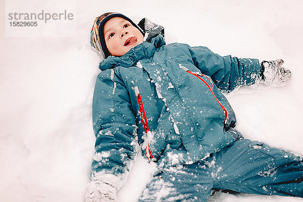 Glücklicher Junge mit ausgestreckten Armen im Winter im Schnee liegend